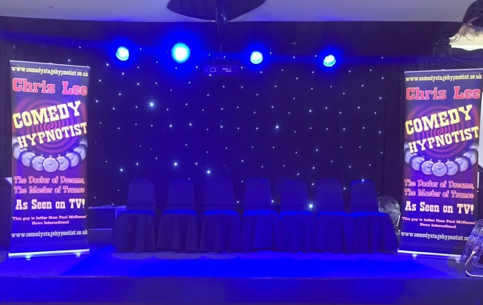 Chris Lee comedy hypnotist stage with volunteer chairs and show banners